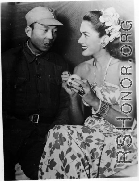 Celebrities visit and perform at Yangkai, Yunnan province, during WWII: Jinx Falkenburg poses with a Chinese soldier while she autographs a tennis ball.