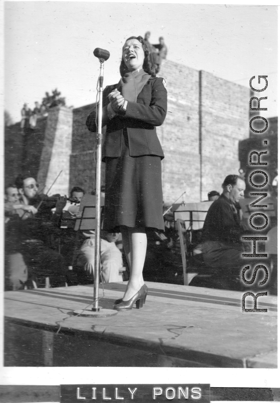 Opera singer Lilly Pons sings at a USO show in Gushkara, India, during WWII.  The boxes in front of the band players are labeled 748th ROB (748th Railway Operating Battalion).
