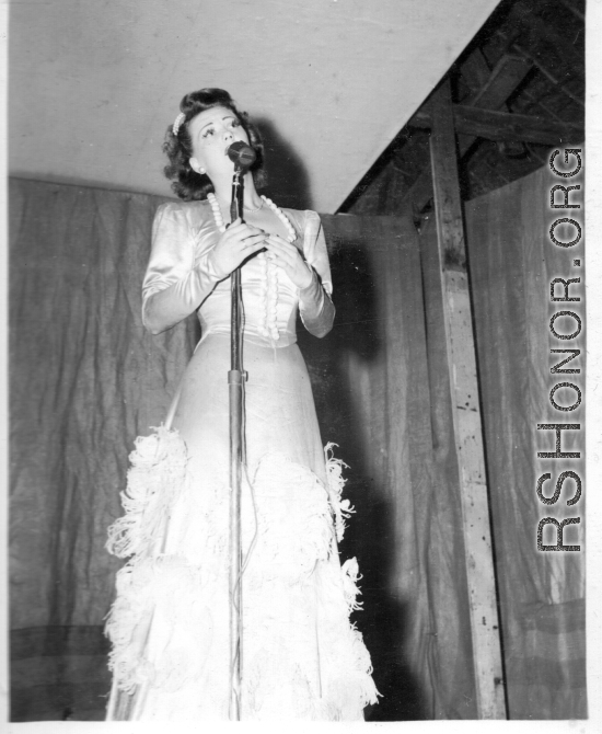Singer at a USO show in Gushkara, India, during WWII.  The boxes in front of the band players are labeled 748th ROB (748th Railway Operating Battalion).