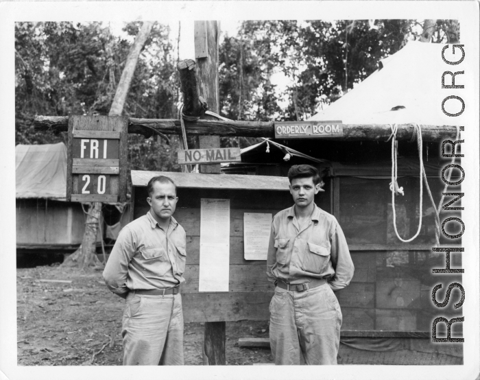 Engineers of the 797th Engineer Forestry Company pose before bulletin board on Friday the 20th, in Burma. On bulletin board is posted a "Buck Sheet," a two page paper printed for GIs in the area. During WWII.
