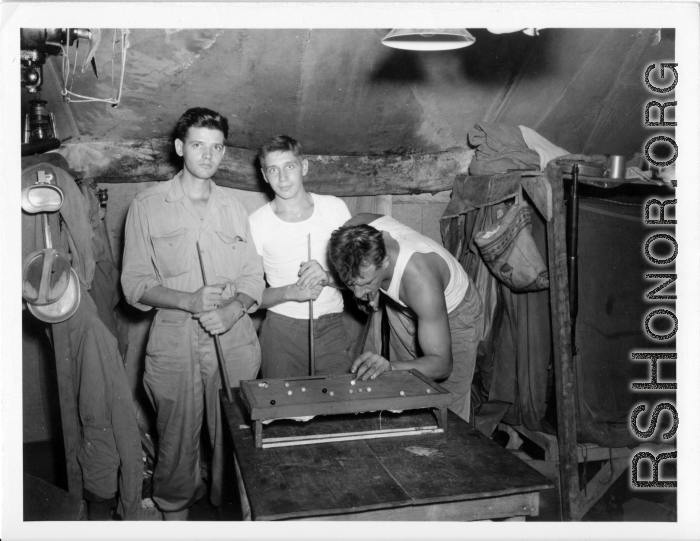 Engineers of the 797th Engineer Forestry Company pose while playing at a tiny pool table in their tent in Burma.  During WWII.