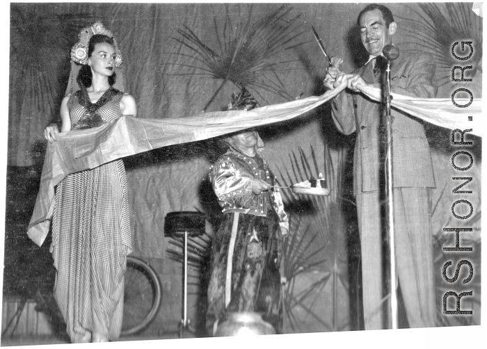 Movie star Melvin Douglas, part of USO troupe, cutting the ribbon during a USO performance at Gushkara, India, during WWII.