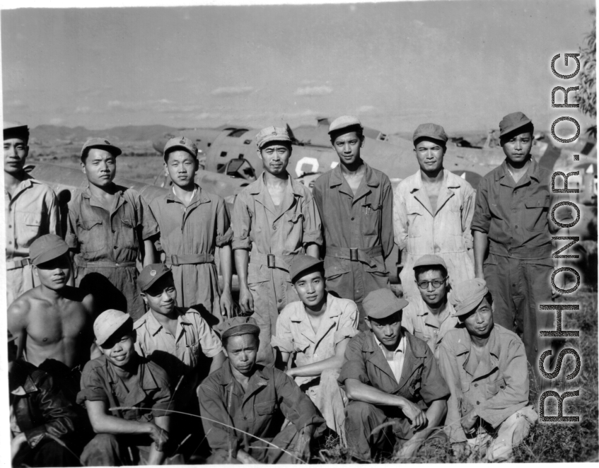 Chinese aircraft mechanics and engineers pose at an air base in China during WWII. Behind them are damaged airplanes used for parts.
