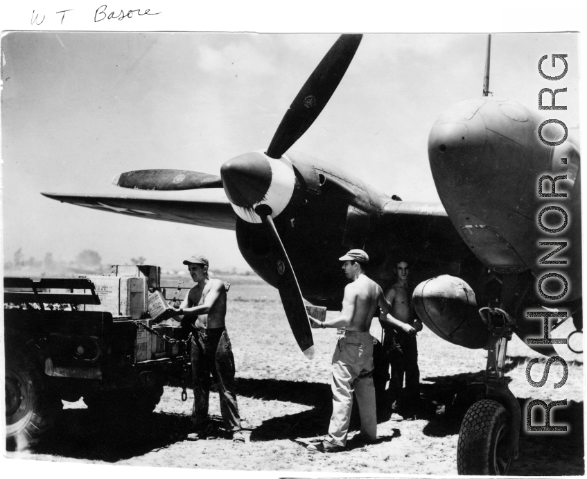 GIs move supplies between a truck and a F-5 (P-38)--not usually considered a cargo carrier--including a box labeled "Curtiss Candy Co." along with cartons of "plum base." In the CBI during WWII.   Photo from W. T. Basore.