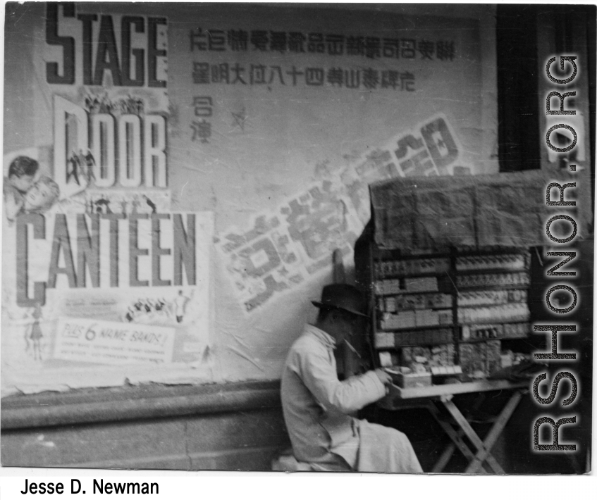 Cigarette vendor in China, set up in front of move advertisement for "Stage Door Canteen" (1943).  Photo from Jesse D. Newman.