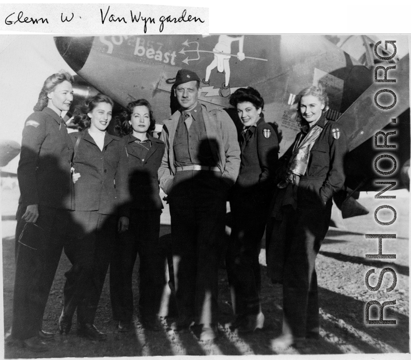 A US flyer surrounded by glamour gals stand in front of US war plane during WWII in the CBI. The plane appears to be a P-38 or F-5, with possible nickname "Sorry Beast."  Photo from Glenn W. Van Wynggarden.