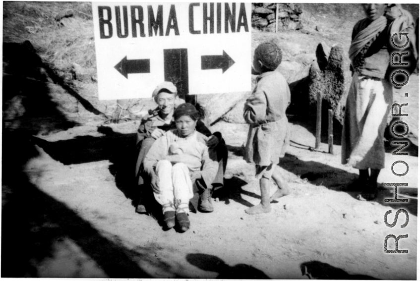 A pipe-smoking GI cuddles a foot-bound Chinese woman against the Burma-China border sign. During WWII.  Image from Emery and Beth Vrana.
