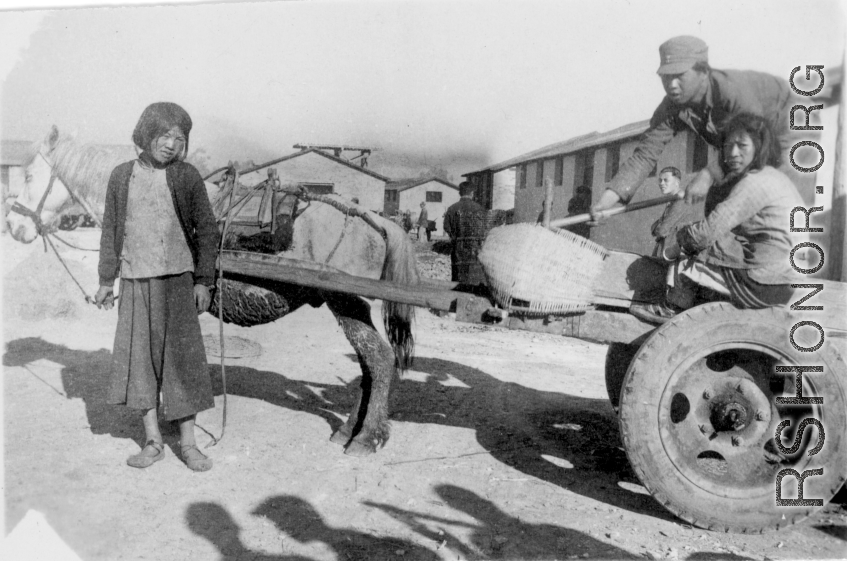Chinese family hauling items by donkey cart  on an American base poses for the camera. In China during WWII.