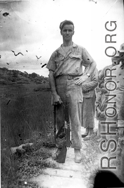Elmer Bukey poses for a photo with some Chinese friends and a Thompson submachine gun, standing by a rice paddy, at Liangshan China, during WWII.