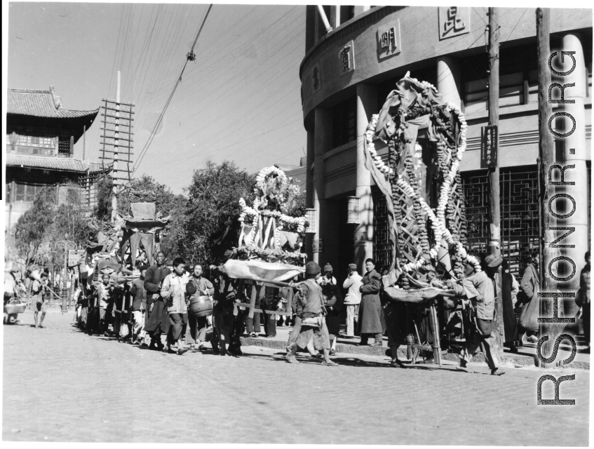 A colorful parade--with floats, marchers, and music--for a local festival in Kunming, China, during WWII.