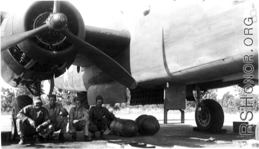 Jim, Frank Bates, Alex, Jim, 1943, in the shade under a B-25. Note large bombs on ground near them.