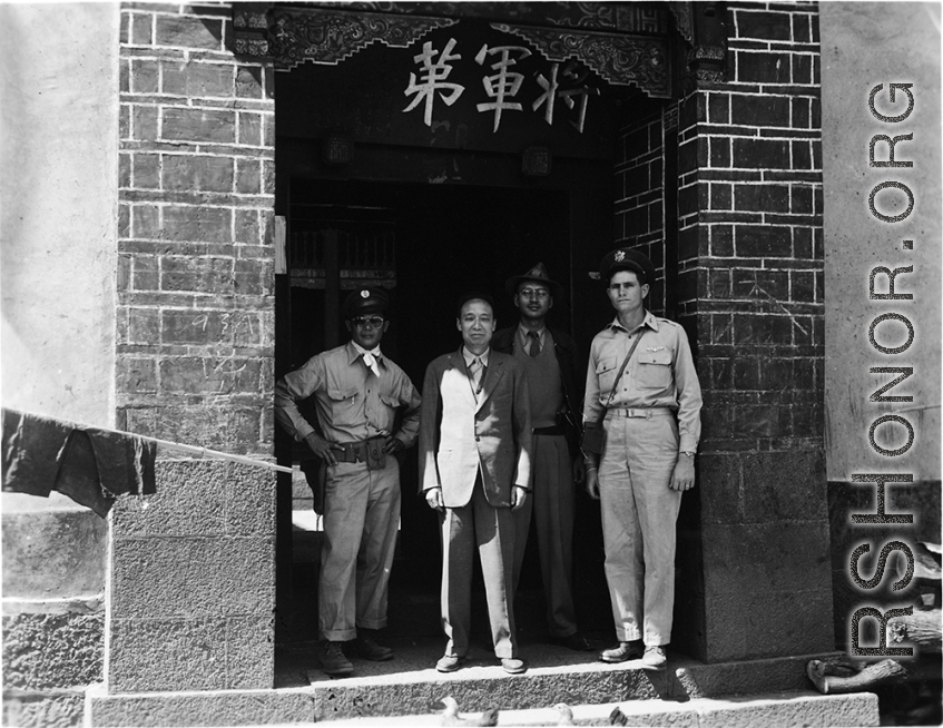 American soldier, KMT solder, and KMT civilians at rally pose for portrait shot. In the suit in the center should be An Zefa (安则法), a highly educated official who had a number of roles in Yunnan during WWII.  These men stand in the gate of an elite residence in Yunnan province, which has been appropriated by Nationalist 5th Corps forces for military purposes--the white paper posted on the door post says the residence is temporary housing for assistant staff for officers, and HQ for an armored unit. The resi