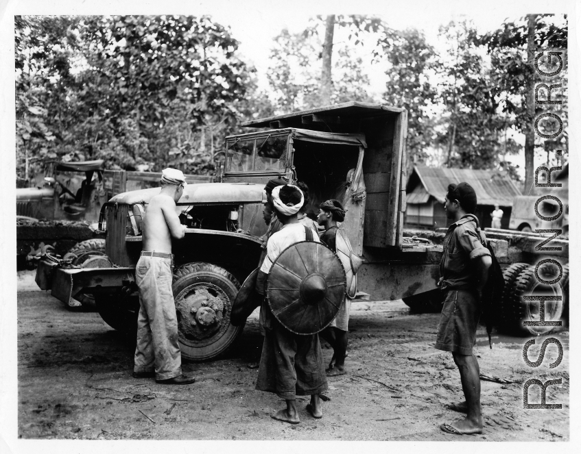 Local men observe as a GI repairs a truck in Burma.  During WWII.  797th Engineer Forestry Company.