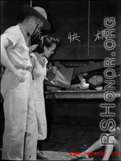 A GI and a local elite pay respects to a refugee at the train station in Liuzhou during WWII, in the fall of 1944, as the Japanese advanced during the Ichigo campaign.