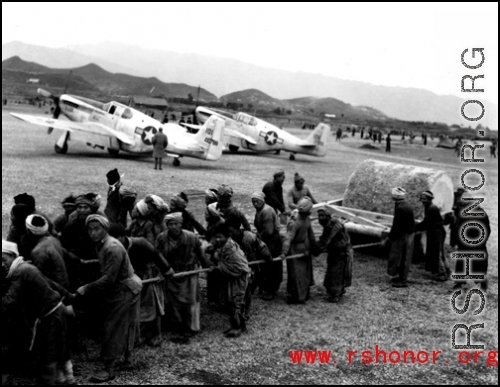 Laborers in China pull a concrete roller at an airbase, with parked P-51 fighters in the background. This was likely in SW China.  From the collection of Hal Geer.