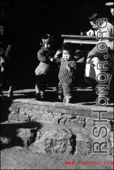 Two toddlers hang out while the adults drink tea at roadside location. In China, during WWII.