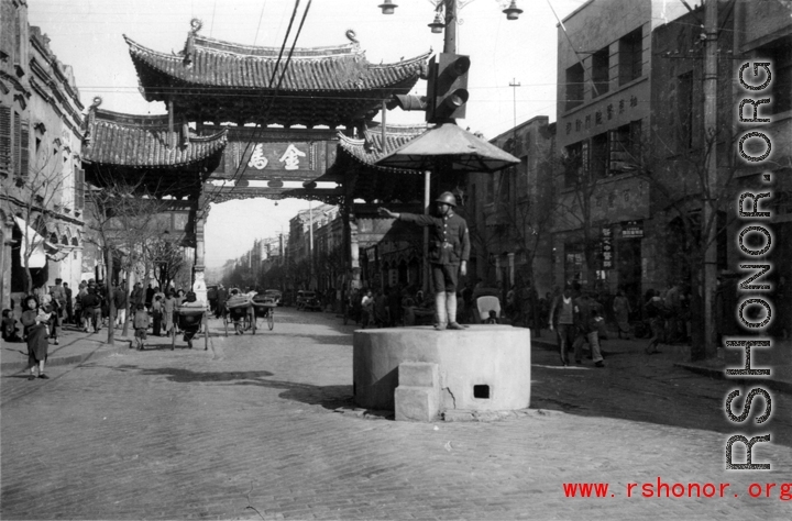 The Golden Horse 金马 archway in Kunming, one of the pair with the Emerald Rooster Archway (金马碧鸡坊) behind the cameraman. A traffic policemen directs traffic from a concrete stand.  In the CBI during WWII.