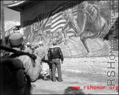 Americans and Chinese stop to look at a large wall mural showing peoples from four countries (China, Britain, United States, Russia, as shown by the four flags) uniting to put fascists in their place.