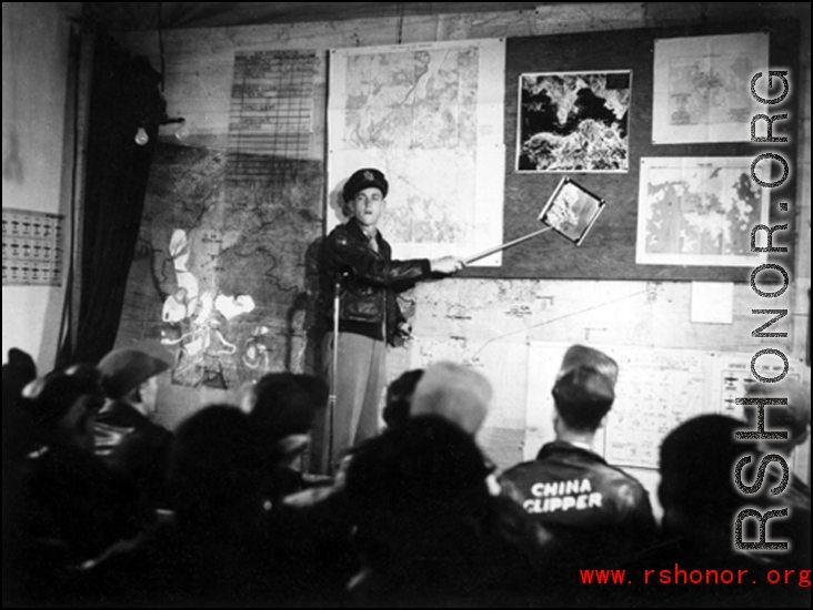 A pre-flight briefing for American flyers in China during WWII.. The maps on the wall behind the speaker clearly show Hong Kong harbor, which the Japanese controlled.