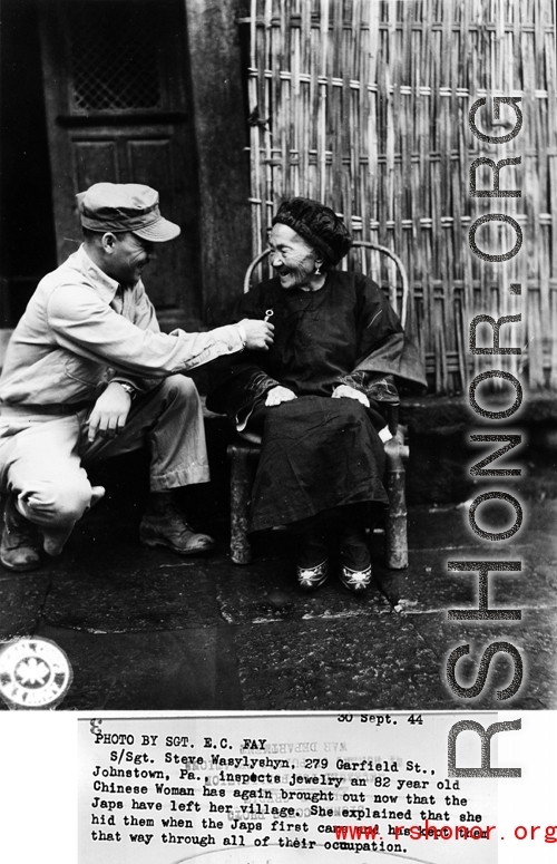 S/Sgt. Steve Wasylyshyn, 279 Garfield St., Johnstown, Pa., inspects jewelry an 82 year old Chinese woman has again brought out now that the Japanese have left her village.  She explained that she hid them when the Japanese first came and has kept them that way through all of their occupation.