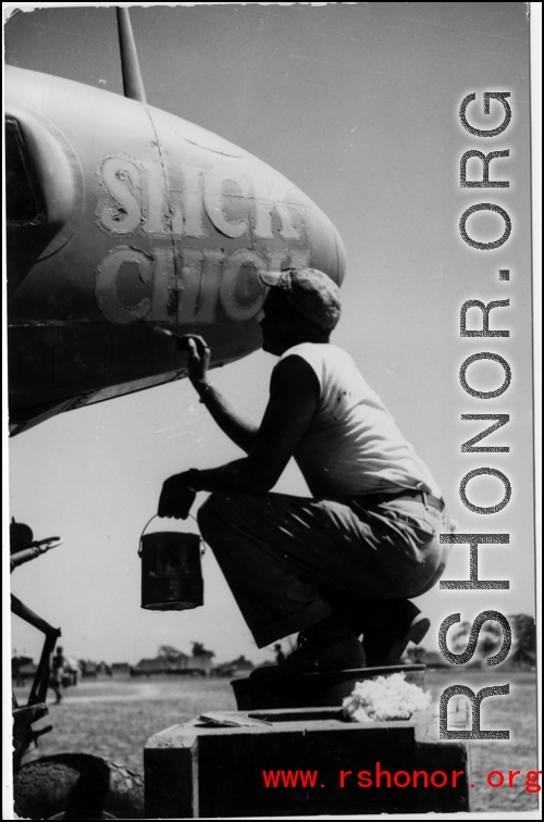 A GI paints the nickname "Slick Chick" on the nose of an aircraft, probably a photo reconnaissance P-38 (note the glass panel for a camera on the bottom of the nose).