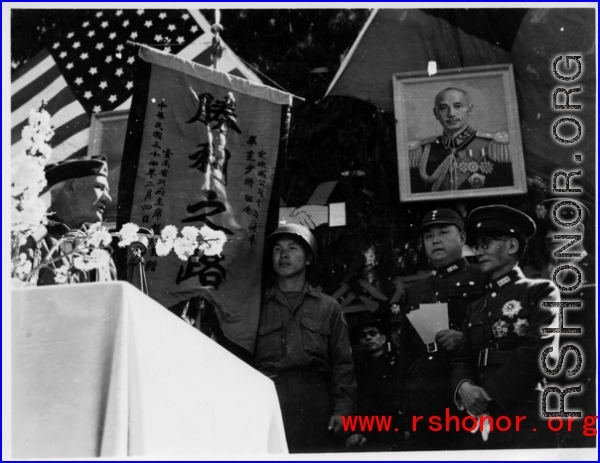Burma Road dedication ceremony in Kunming, China, on February 4, 1945, during WWII. Review of first convoy (or one of the first convoys) to reach China. General view of the stage and reviewing party, with American and Chinese dignitaries, soldiers, and civilian VIPs. An American band plays, and an honor lines on both sides of the center carpet stand in formation.  Official dignitaries at the ceremony included, on the Chinese side, such figures as General Lung Yun, Governor of Yunnan Province,  Gen. Wang Yu-