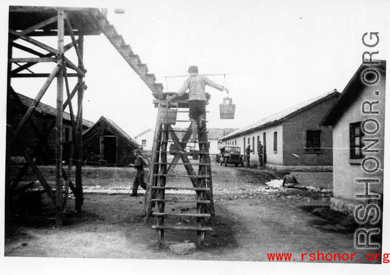 Worker fills water tank at an American base in Yunnan, China, during WWII, by climbing up stairs carrying pails of water.