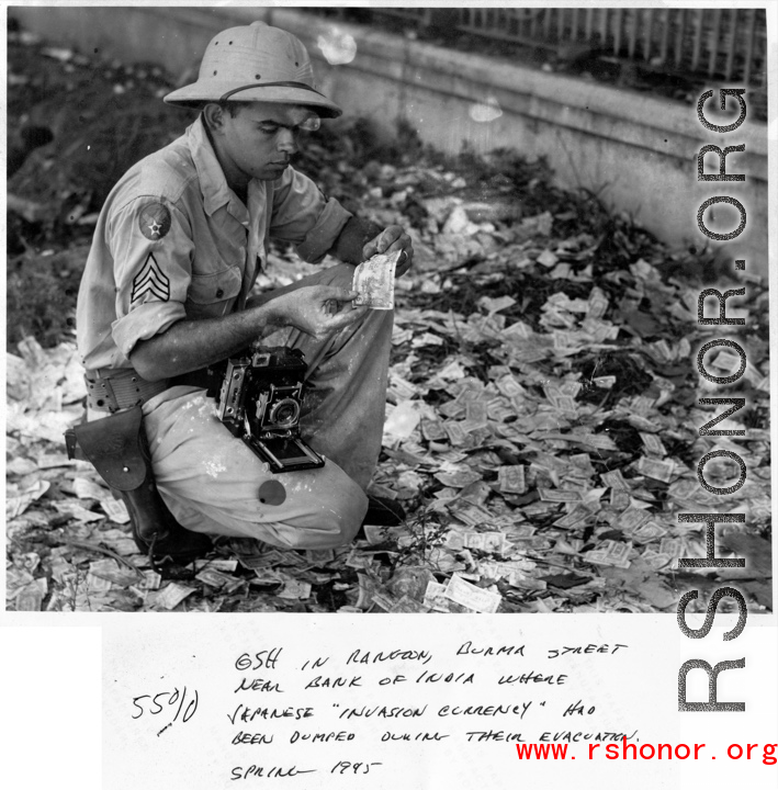 GI examines discarded "invasion currency" on a Rangoon, Burma, street near Bank of India, where it had been dumped during evacuation. Spring 1945.