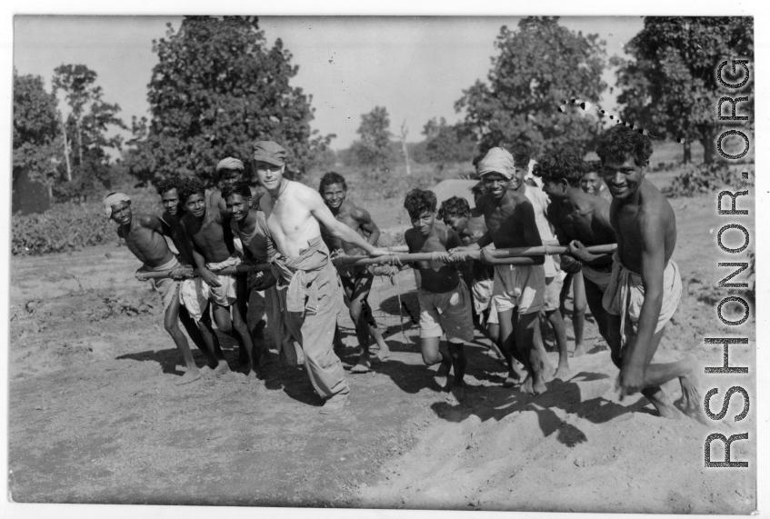 To get a great photo, a GI lends a hand to Indian work crew to pull concrete roller.  Scenes in India witnessed by American GIs during WWII. For many Americans of that era, with their limited experience traveling, the everyday sights and sounds overseas were new, intriguing, and photo worthy.