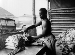 An African-American serviceman carefully packs a parachute for use by aircrews in emergency bailouts, in some location in the CBI where the weather was hot.