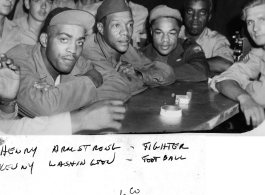 African-American servicemen in a club or bar in Myitkyina in 1945, during WWII. Stars in pre-army life, the fighter Henry Armstrong and the football player Kenny Washington get full attention from surrounding fans.