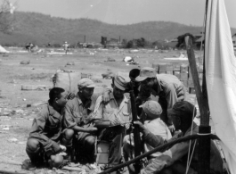 On the ground in the midst of air drop parachutes, a GI coordinates with a group of Chinese soldiers.