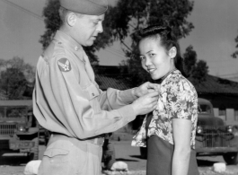 Miss Ulian Hhoo of Singapore receives the Meritorious Civilian Service Award from Col. Richard H. Wise for her work with the American Army in China. Since August 1943 she had worked in the office of a sector surgeon as typist for the medical supply section, laboratory technician, and surgical nurse in the base dispensary operating room.