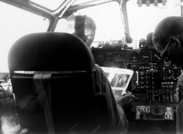 Col. Hopson reading and smoking a cigarette in B-24 cockpit in flight back to US after end of war in the CBI. This is B-24 #44-51040.