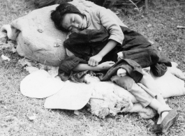 A woman sleeping, possibly cradling a baby: A tired, sick, or weakened refugee during the Chinese civilian evacuation in Liuzhou city, Guangxi province, China, during WWII, in the summer or fall of 1944 as the Japanese swept through as part of the large Ichigo push.