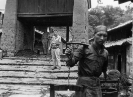 GIs go through village in Yunnan province, probably Yangkai village, carbines over shoulder, while local people go about their regular business. During WWII.