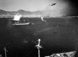 B-25 pulls up after run on Japanese shipping in Hong Kong harbor, while the photographer's B-25 scims just above Japanese cargo ship.