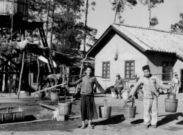 GI explorations of the hostel area at Yangkai air base during WWII: Men haul water in barrels on shoulder poles for use in the hostels.