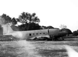A man in pith hat stands of fuselage remains of a C-47 transport next to railroad track. In the CBI during WWII.
