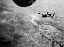 A B-24 flying with smoke billowing up behind from recent bombing, in the CBI, during WWII.
