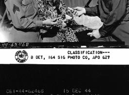 Major Robert E. Envell offering a taste of peanut candy now locally manufactured and sold for GI's in the PX's at APO 627 to Sgt. Claude S. Merrill and his escort.  December 15, 1944.  Photo by Pfc. Thomas F. Melvin. 164th Signal Photographic Company, APO 627.  Passed by Emanuel Goldberg.