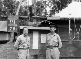 Engineers of the 797th Engineer Forestry Company pose before bulletin board on Friday the 20th, in Burma. On bulletin board is posted a "Buck Sheet," a two page paper printed for GIs in the area. During WWII.