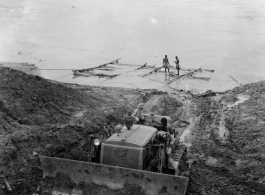 Cat pulling logs raft up bank from river.  797th Engineer Forestry Company in Burma.  During WWII.