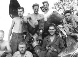 Boys of the 2005th Ordnance Maintenance Company, 28th Air Depot Group, sitting of the engine of a wrecked airplane, in Burma. During WWII. One is holding a puppy--their "mascot" named "Evan." John Schuhart sitting cross-legged with cigarette. 
