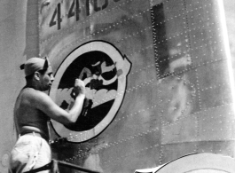 Unknown artist painting "The Wily Wolves" squadron insignia on tail of 24th Combat Mapping Squadron F-7, #441680.