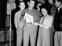 A group of Americans and two Chinese prepare to sing off a sheet of paper into a microphone.