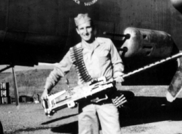 Robert Fox holds a heavy machine gun in front of a B-25 of the Ringer Squadron.