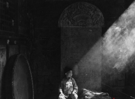 During WWII a boy sits in front of a stone tablet in the entry area of a temple or other building, probably in Yunnan province.