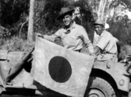 Ival Baker shows souvenir captured Japanese flag, while his bodyguard watches on. During WWII, in China.  Photo from Ival Baker.