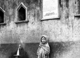 A child at a public well in the Darjeeling, India, area. Readable on the sign above are the words in English "TO THE GLORY OF GOD." During WWII.  Photo from Robert D. Lichty.